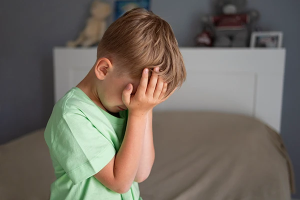 Young boy covering his face in distress, showing signs of childhood anxiety.