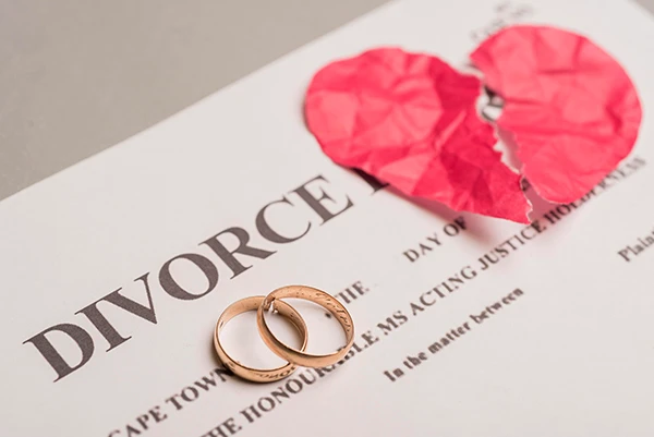 Divorce papers with wedding rings and a torn paper heart, representing family transitions.