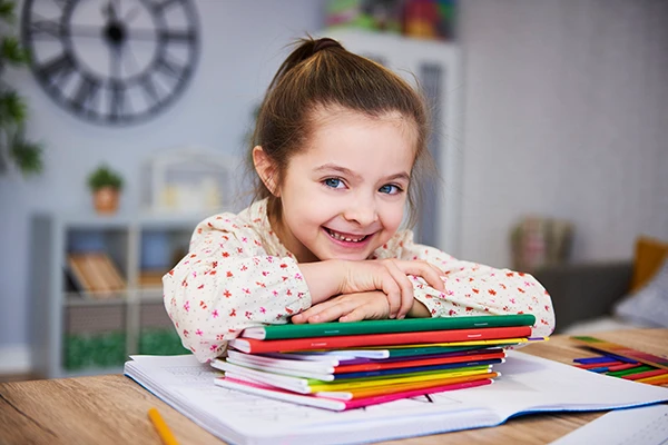 Smiling young girl leaning on a stack of colorful school notebooks, feeling calm and confident.
