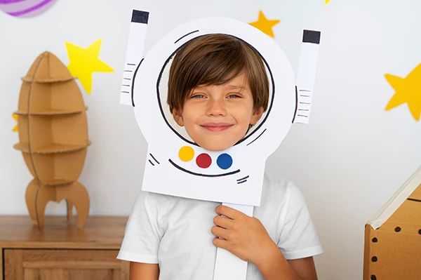 Smiling boy holding a paper astronaut helmet cutout during creative play to help manage child anxiety.