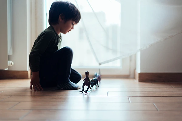 Young boy lining up toy dinosaurs on the floor, engaging in quiet play to manage anxiety.