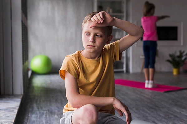 Young boy looking stressed and overwhelmed with hand on forehead, showing signs of childhood anxiety.