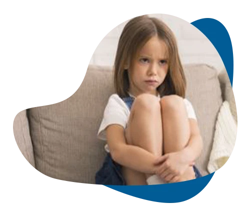 Sad young girl sitting curled up on a couch, showing emotional distress from childhood trauma.
