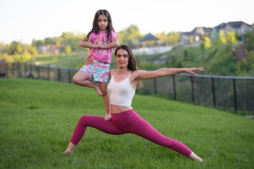 Woman and young girl practicing outdoor partner yoga poses for children's mindfulness and movement.
