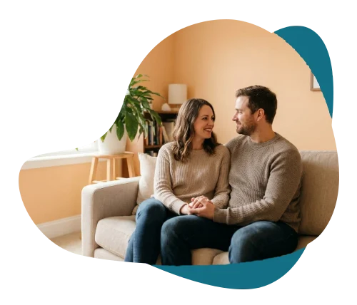 Couple holding hands and smiling at each other on a sofa, representing couples counselling in Richmond Hill.