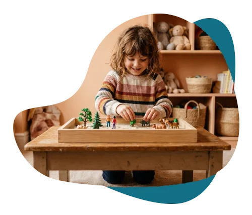 Smiling girl arranging miniature figures in a sand tray during play therapy for kids in Richmond Hill.